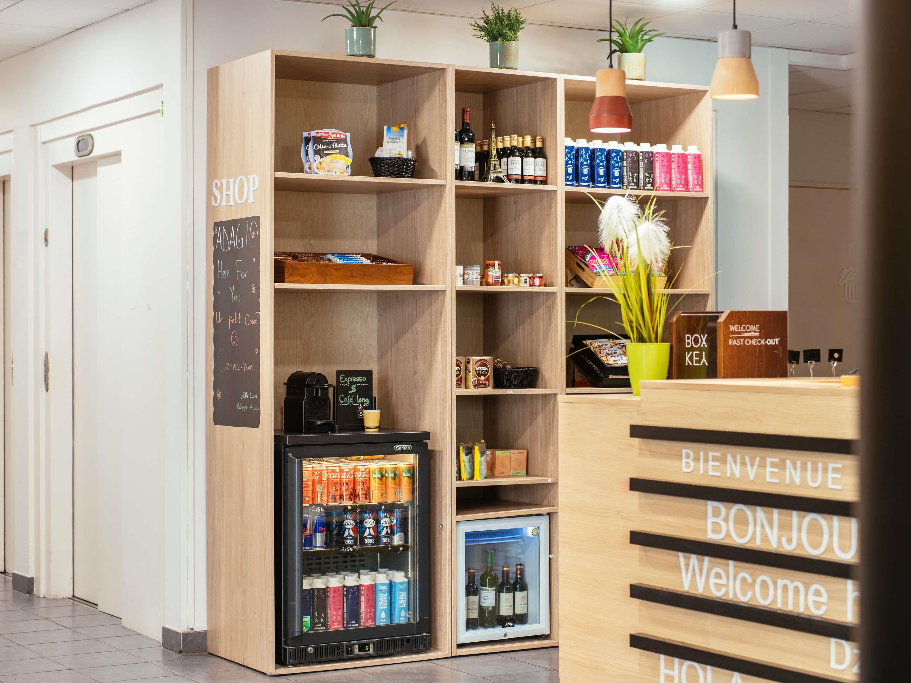 Un espace d’accueil moderne, doté d’un comptoir de réception en bois, d’un réfrigérateur pour les boissons et d’étagères remplies de collations et de condiments.