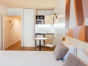 A compact hotel room with a bed, a small round table, a microwave, and a kitchenette.