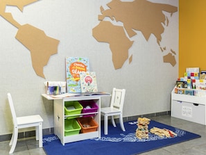 A children's play area with a white desk, colorful storage bins, and a world map on the wall.