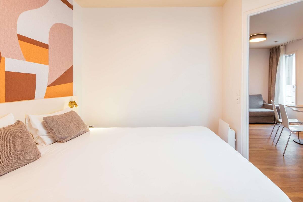 Une chambre d’hôtel avec un grand lit, une œuvre d’art murale et une vue sur la salle à manger.