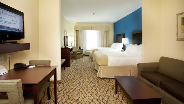 A hotel room with a bed, a desk with a computer, a television, a sofa, and a patterned carpet. - Holiday Inn Express Hotel & Suites Bossier City - Louisiana by IHG (Bossier City)