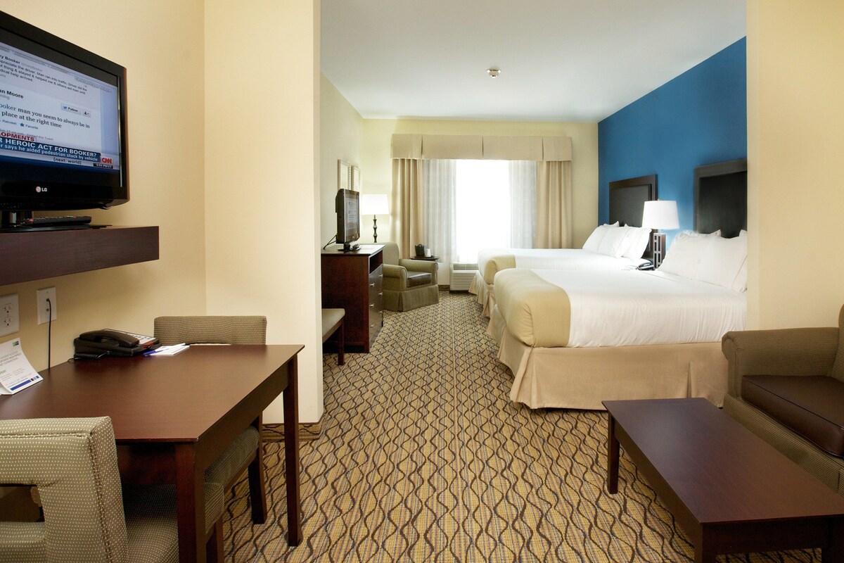 A hotel room with a bed, a desk with a computer, a television, a sofa, and a patterned carpet.