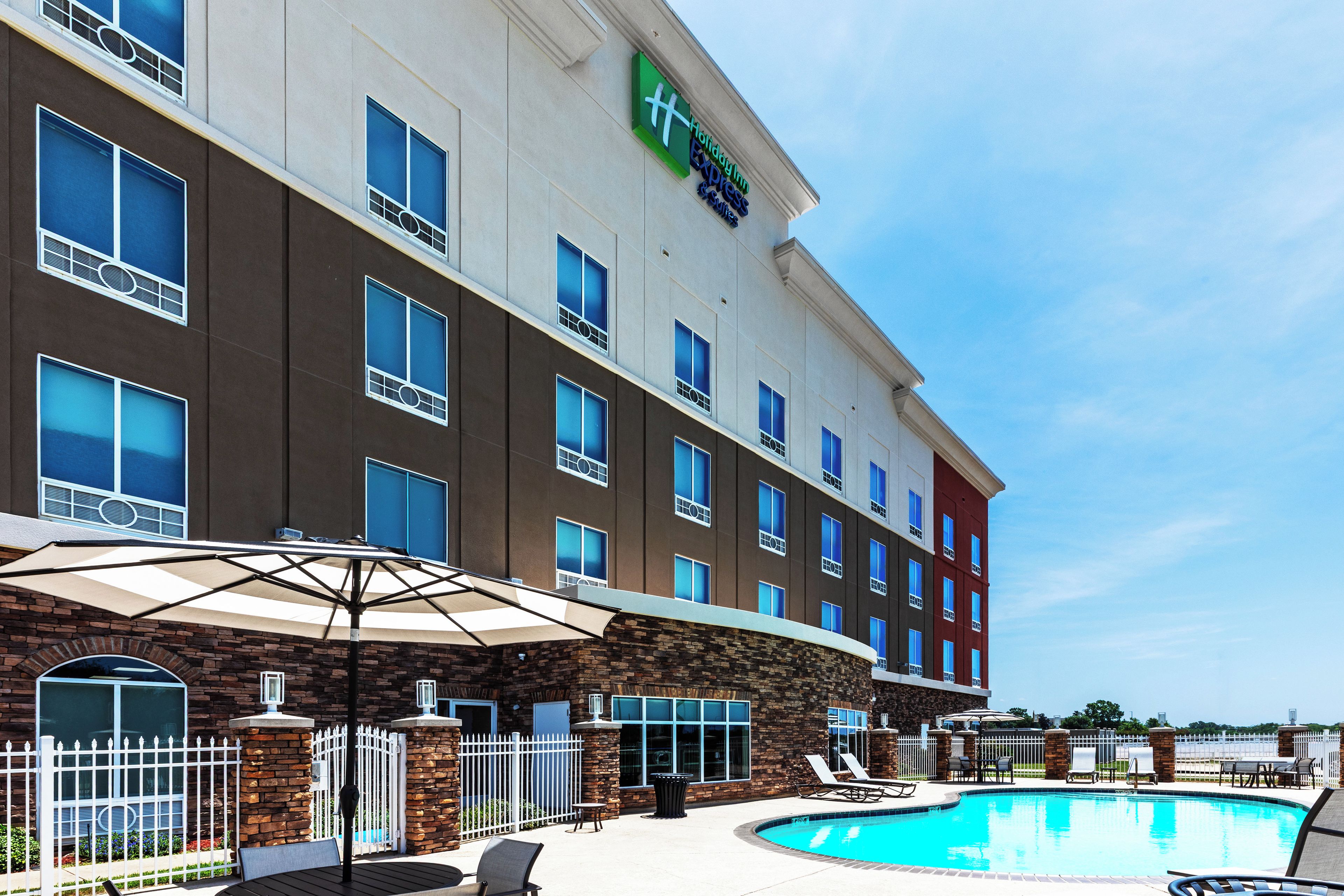 A hotel with a swimming pool, outdoor seating, and a clear blue sky.