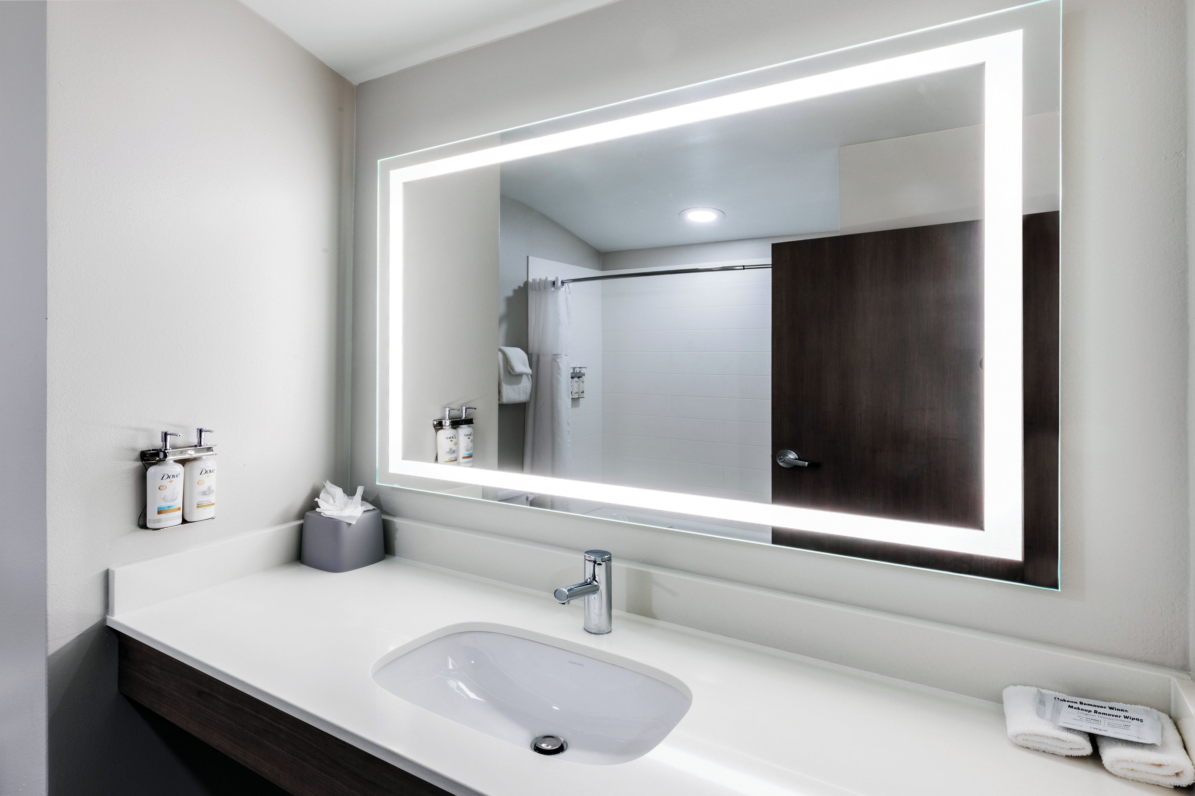 A modern bathroom with a large mirror, a sink, and toiletries.