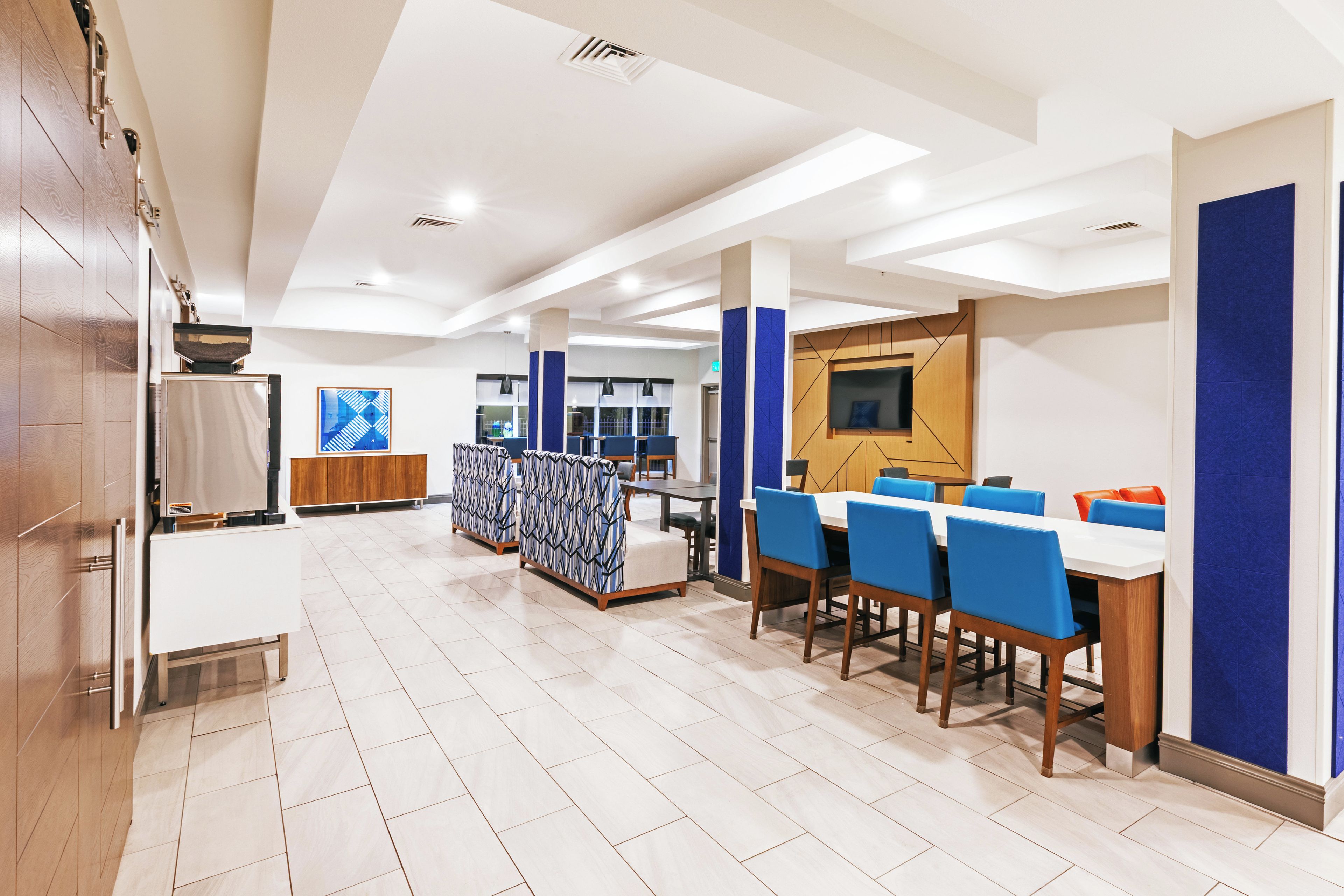 A modern hotel dining area with a long table, blue chairs, and a patterned partition.