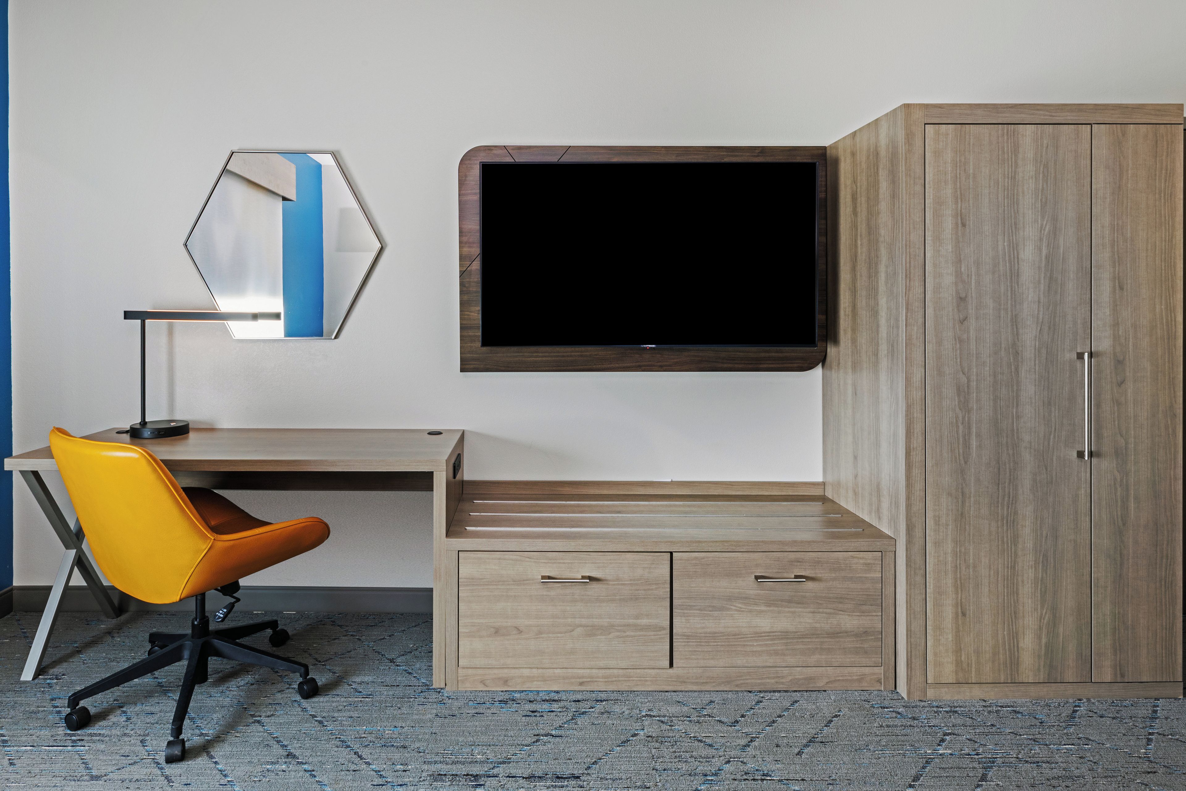 Une pièce comprenant un bureau, un fauteuil de bureau orange, un téléviseur à écran plat fixé au mur et une armoire en bois.