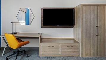 Une pièce comprenant un bureau, un fauteuil de bureau orange, un téléviseur à écran plat fixé au mur et une armoire en bois.