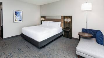 A hotel room with a bed, a chair, a nightstand, a lamp, and a wall-mounted light fixture.