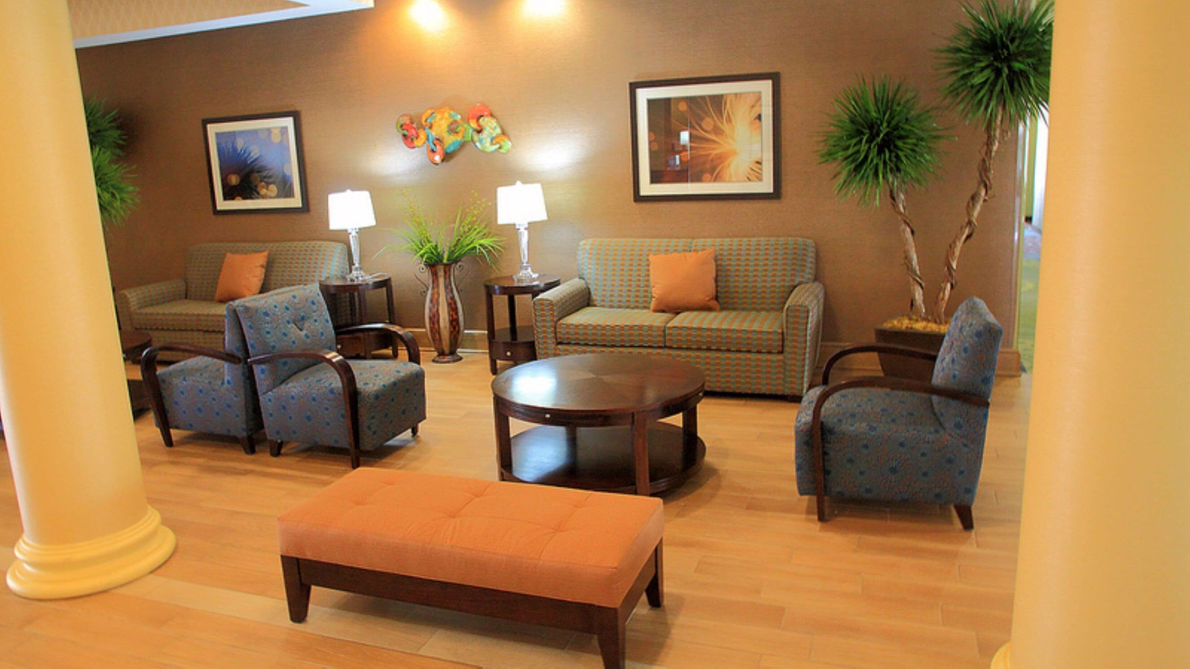 A furnished living room with a sofa, chairs, a coffee table, and a bench. There are two lamps, a potted plant, and framed artwork on the walls.