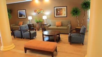 A furnished living room with a sofa, chairs, a coffee table, and a bench. There are two lamps, a potted plant, and framed artwork on the walls.