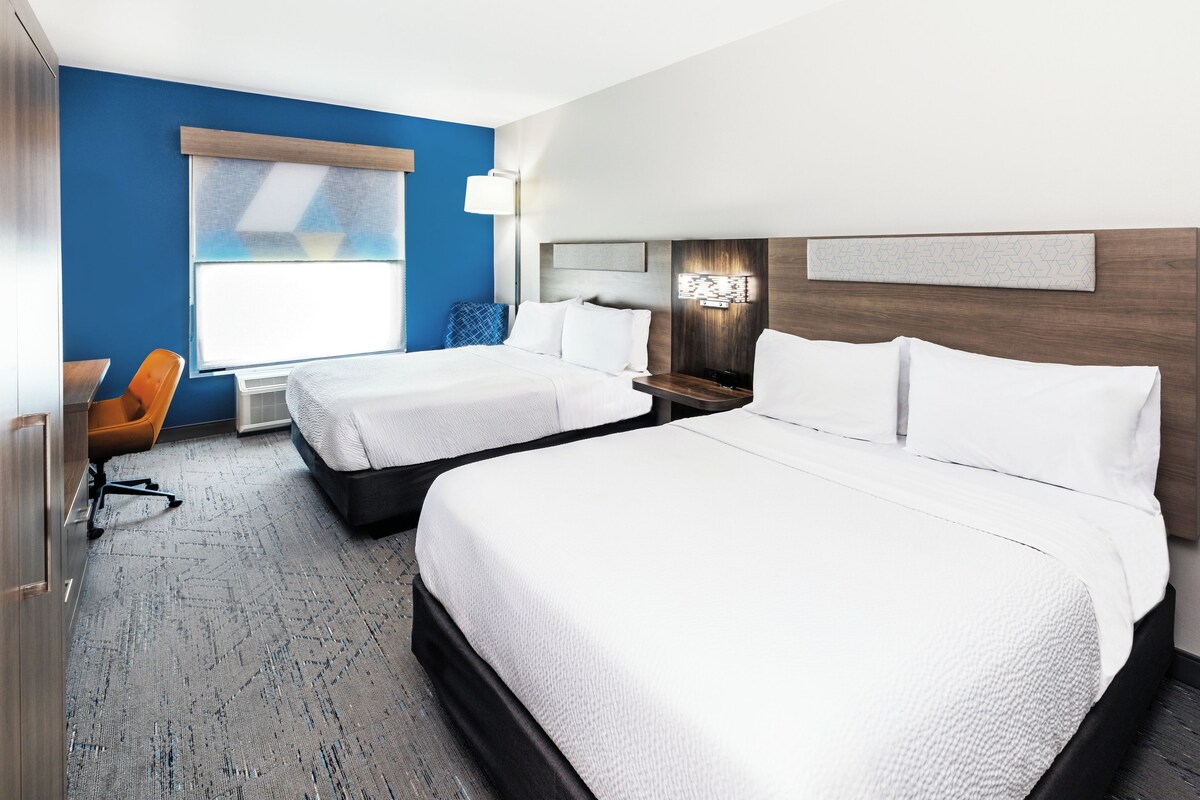 A hotel room with two beds, a desk, a chair, and a window.