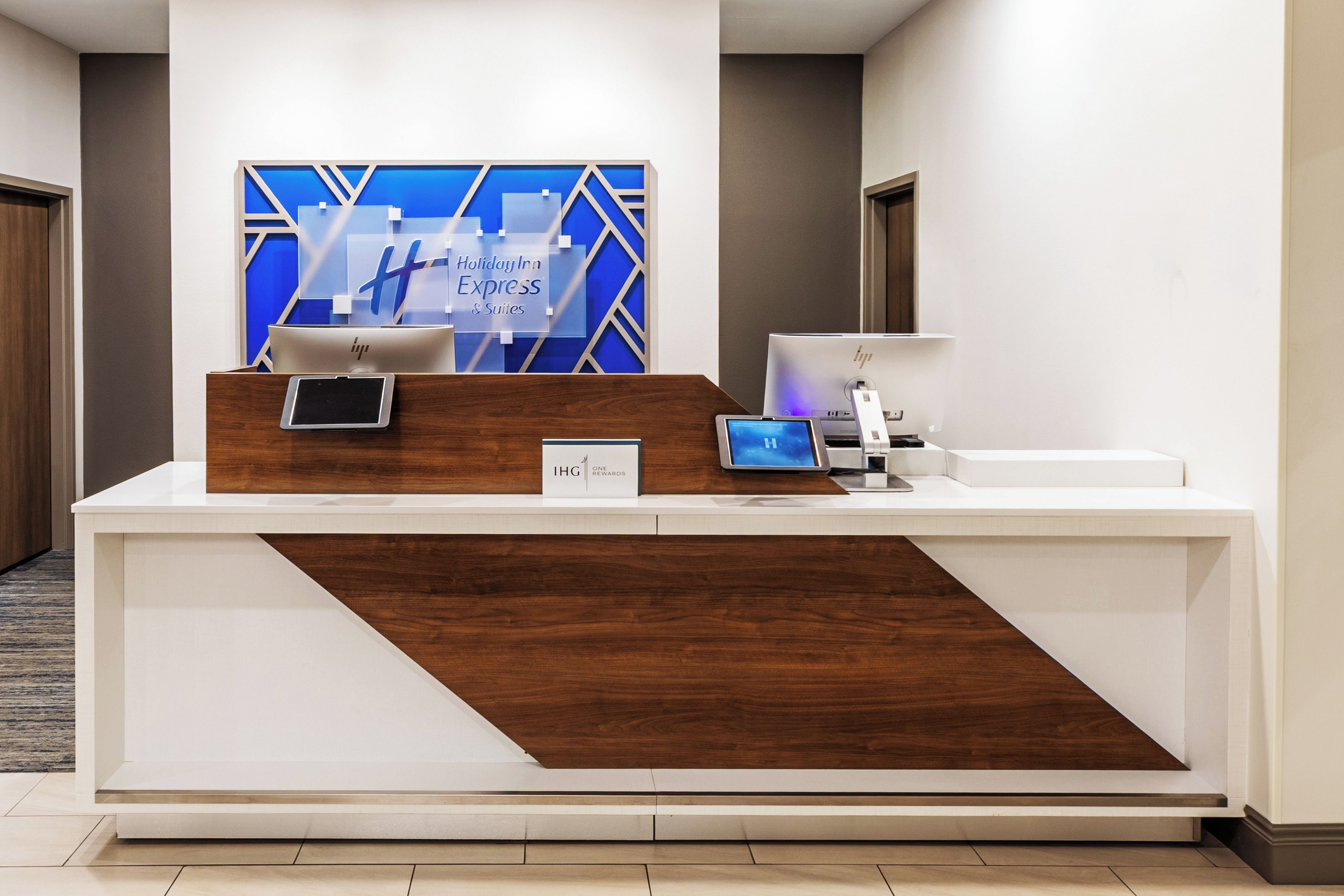 Un comptoir d’accueil d’hôtel au design moderne, comprenant un écran numérique, une tablette et une imprimante.
