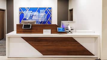 Un comptoir d’accueil d’hôtel au design moderne, comprenant un écran numérique, une tablette et une imprimante.