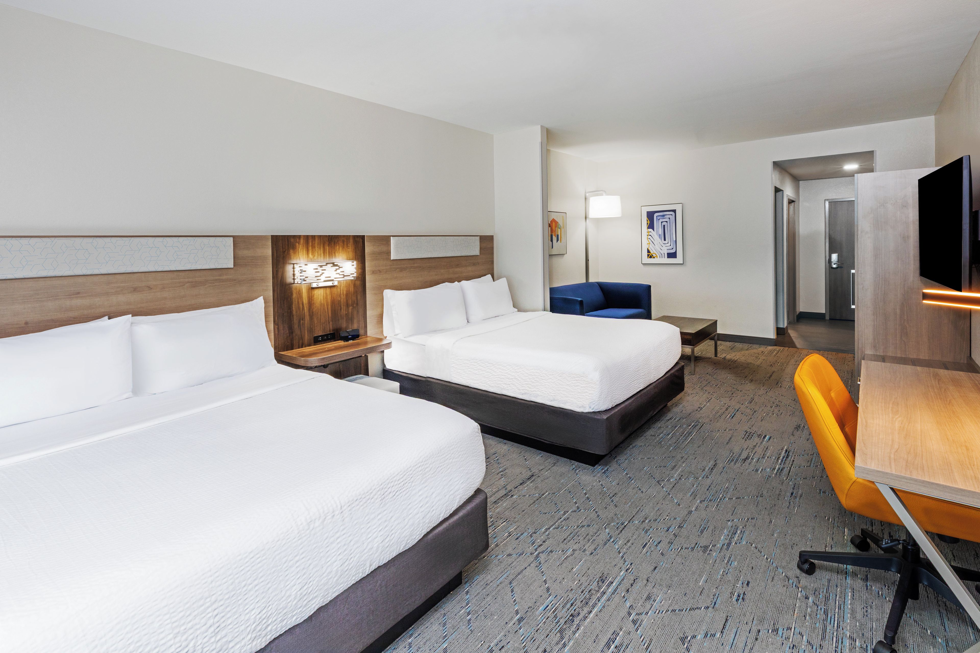 A hotel room with two beds, a desk, a chair, and a television.