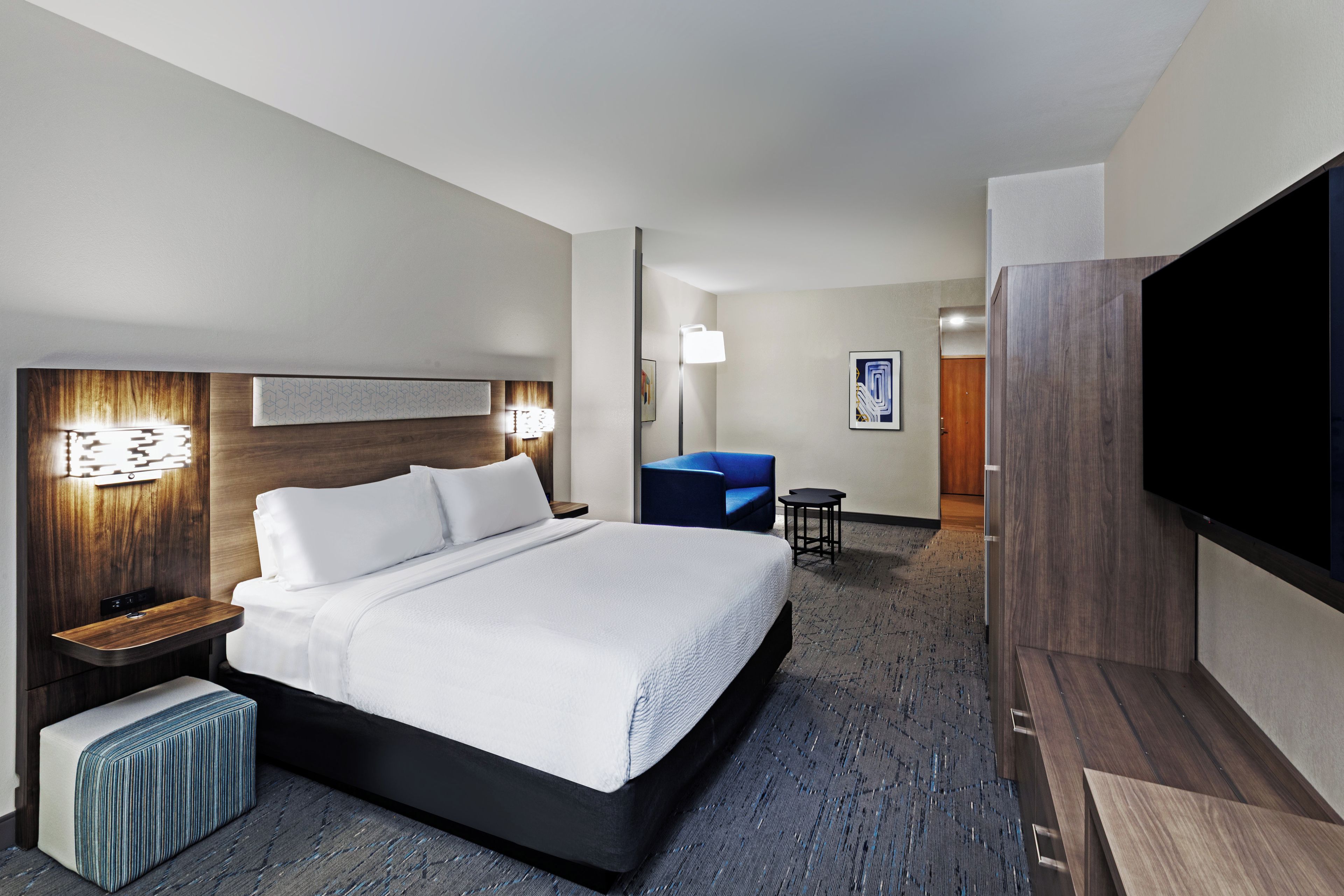 A hotel room with a bed, bedside tables, a desk, a chair, a TV, and a wall-mounted artwork.