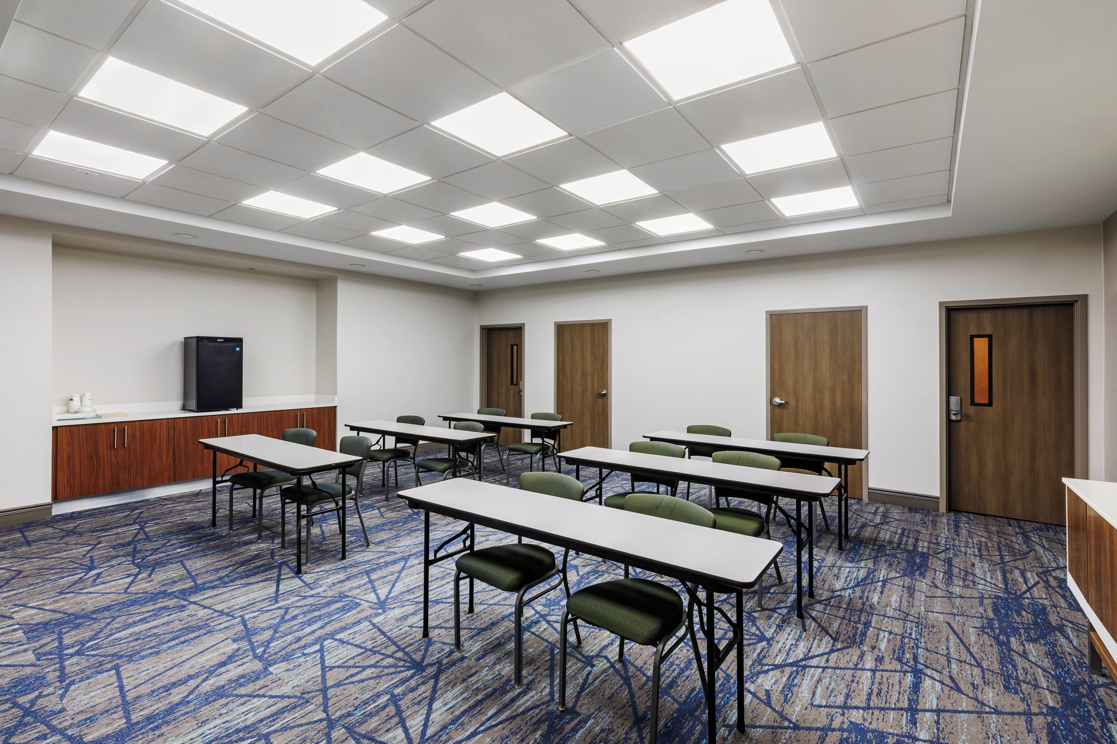 Une salle de conférence équipée de plusieurs tables et chaises, d’un coin cuisine et d’une porte dotée d’une poignée.