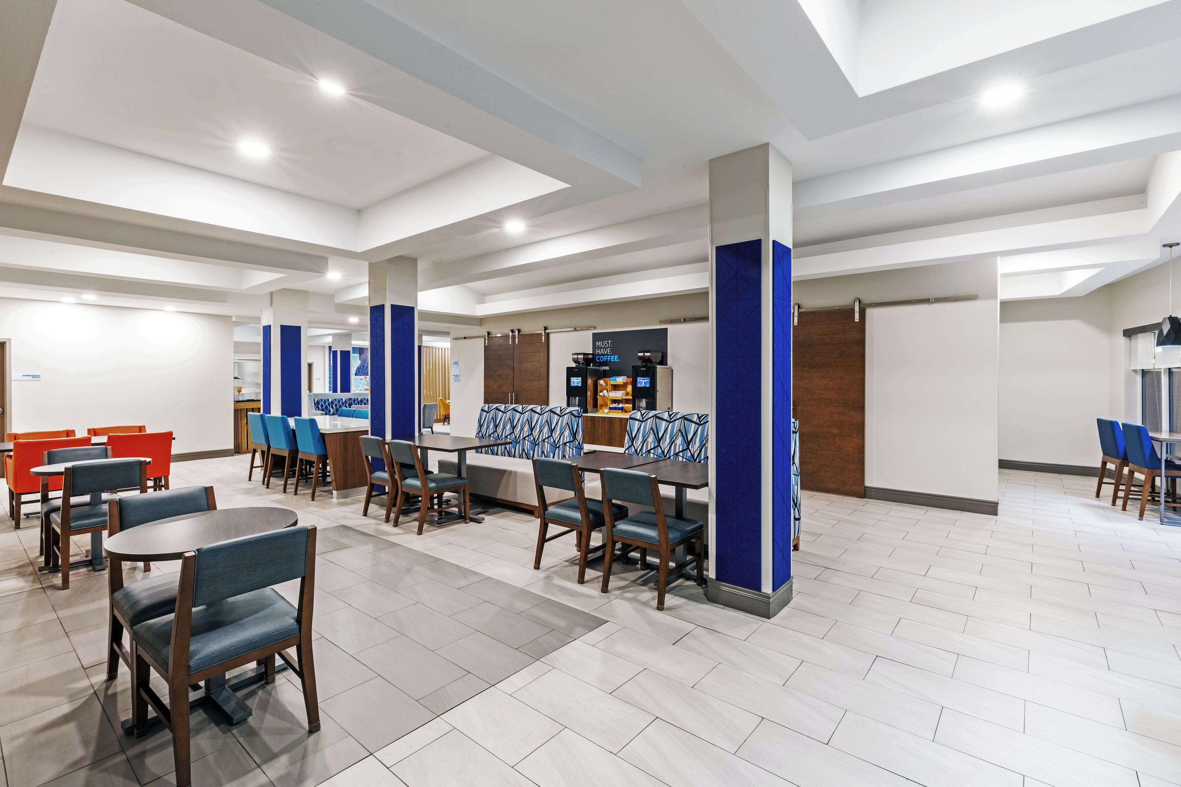 A hotel lobby with multiple seating areas, including tables and chairs, and a coffee station.