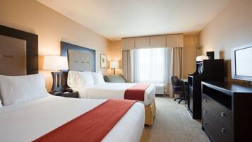 A hotel room with two beds, a desk, a chair, a television, and a window with curtains.