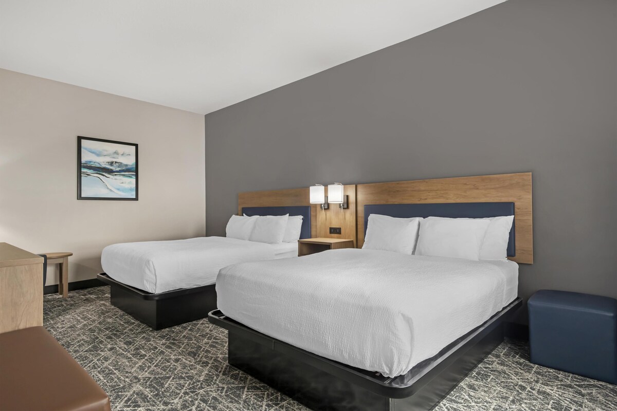 A hotel room with two beds, a desk, and a chair.