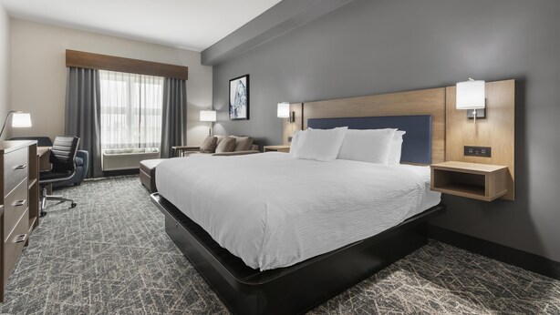 A hotel room with a large bed, a desk, a chair, and a window with curtains.