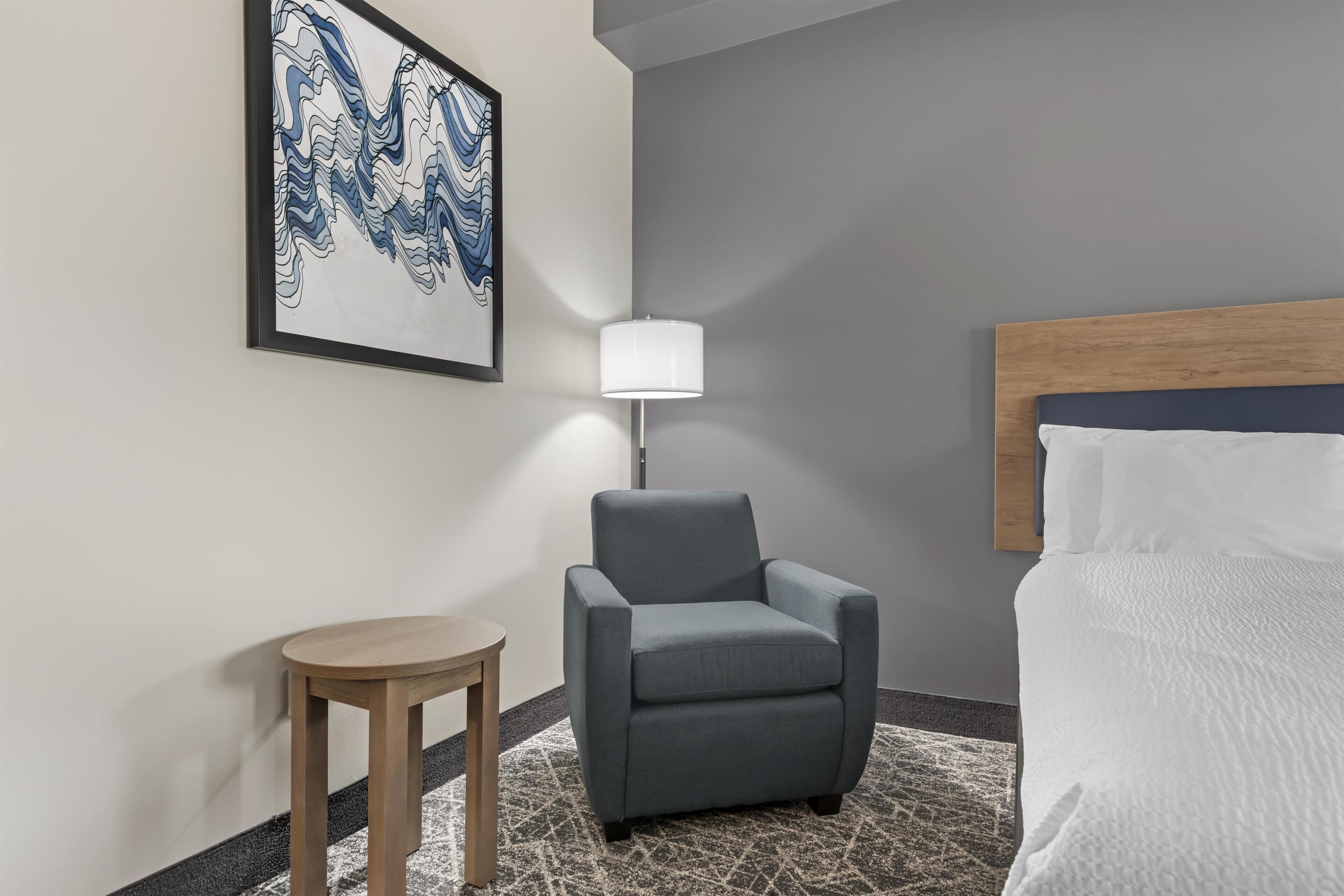 Ein Hotelzimmer mit einem Bett, einem Sessel, einem kleinen Tisch, einer Lampe und einem Wandbild.