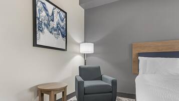 A hotel room with a bed, a chair, a small table, a lamp, and a wall art piece.