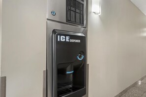 Un distributeur de glaçons fixé au mur, doté d’un bouton-poussoir et d’un logo circulaire placé au-dessus.