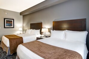 A hotel room with two beds, a nightstand with a lamp, a framed picture on the wall, and a carpeted floor. - Best Western Plus Brandon Inn (Brandon)