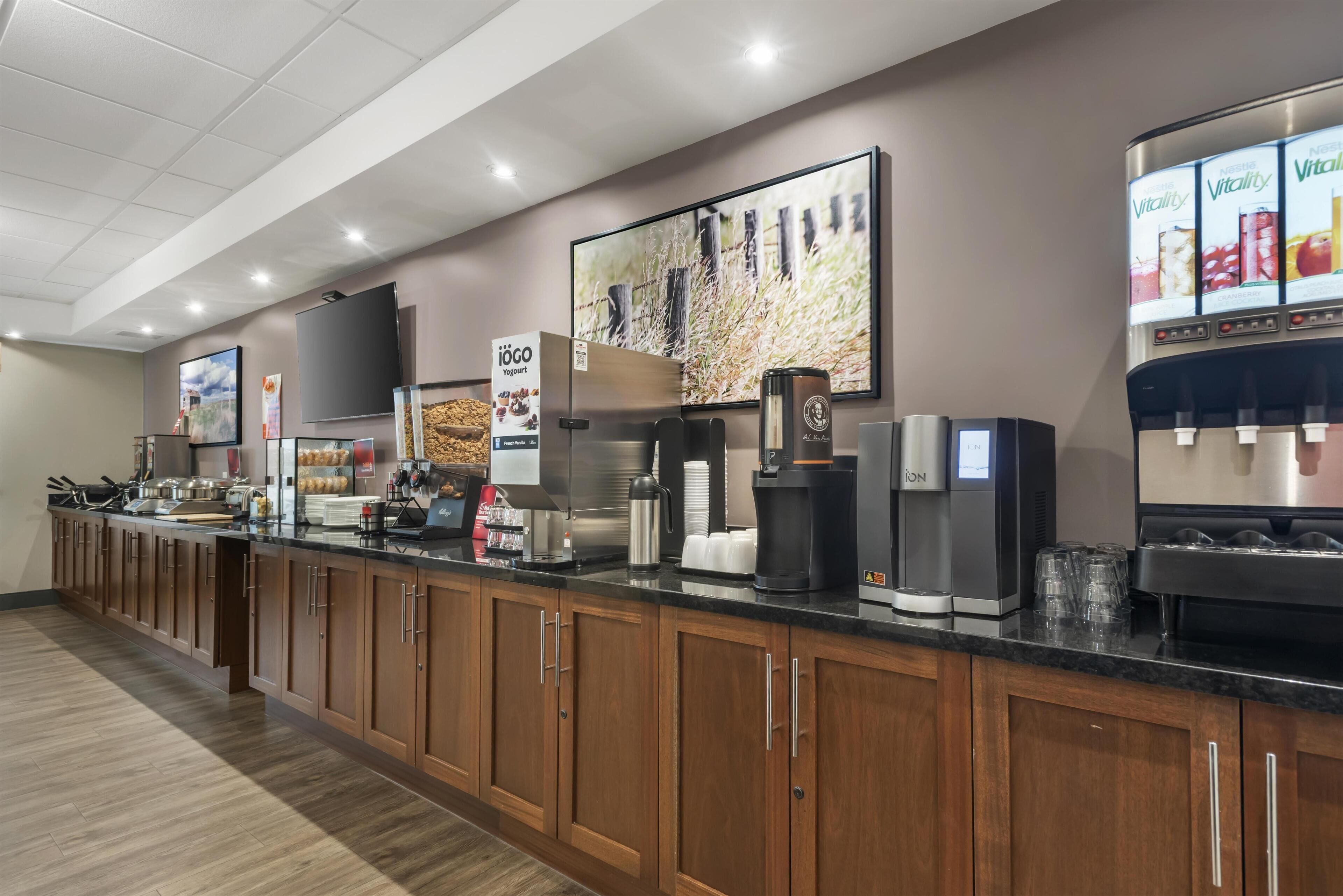 A hotel breakfast area with a long counter, coffee machines, and a refrigerator.