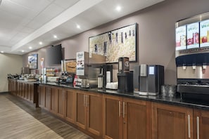 A hotel breakfast area with a long counter, coffee machines, and a refrigerator.