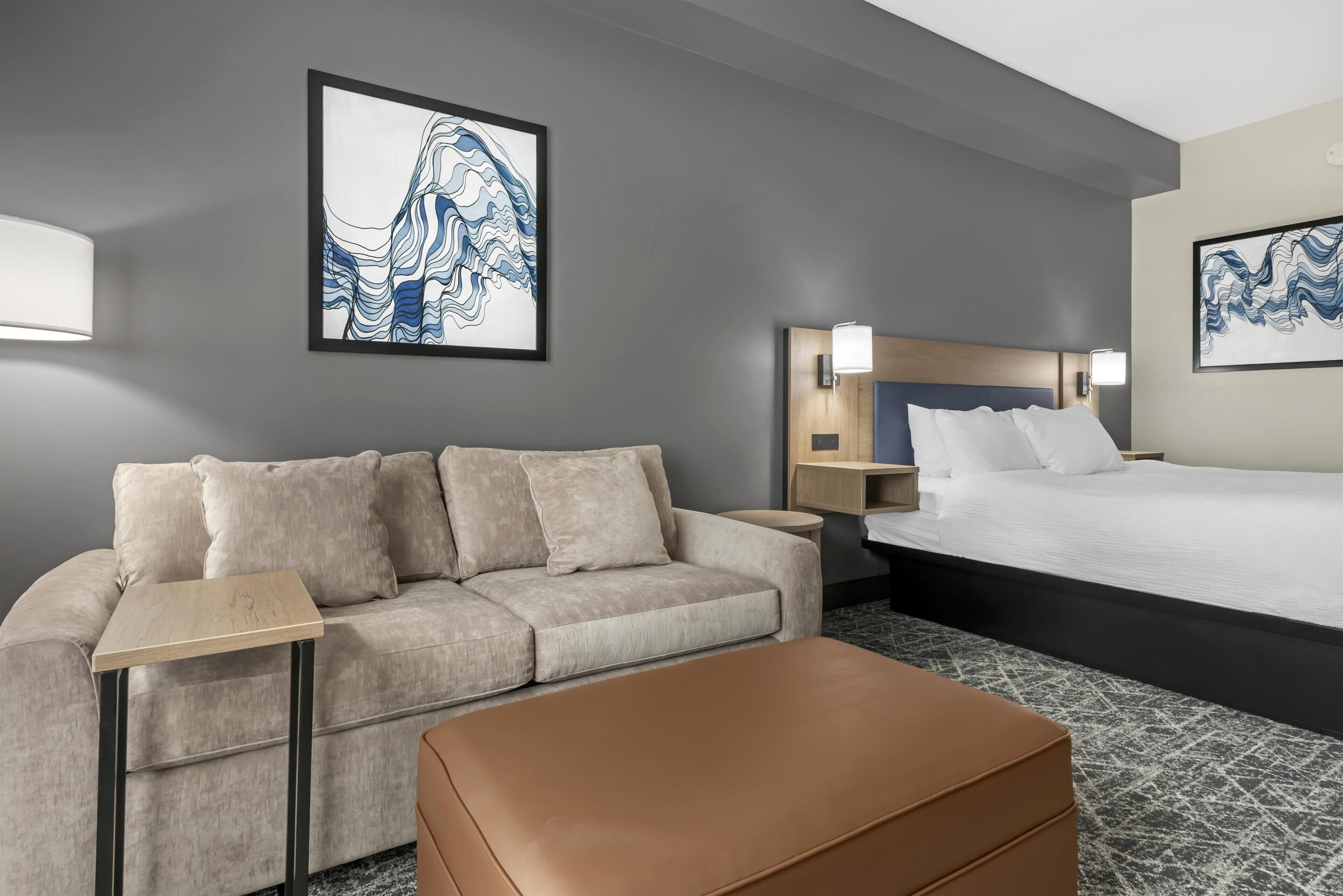 A hotel room with a bed, a sofa, a small table, and two wall-mounted lamps.