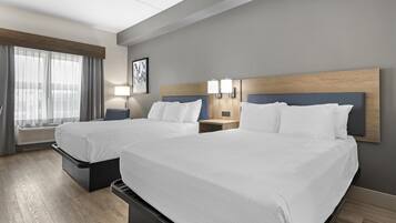 Een hotelkamer met twee bedden, een groot raam met gordijnen, een kunstwerk aan de muur en een nachtkastje met een lamp.