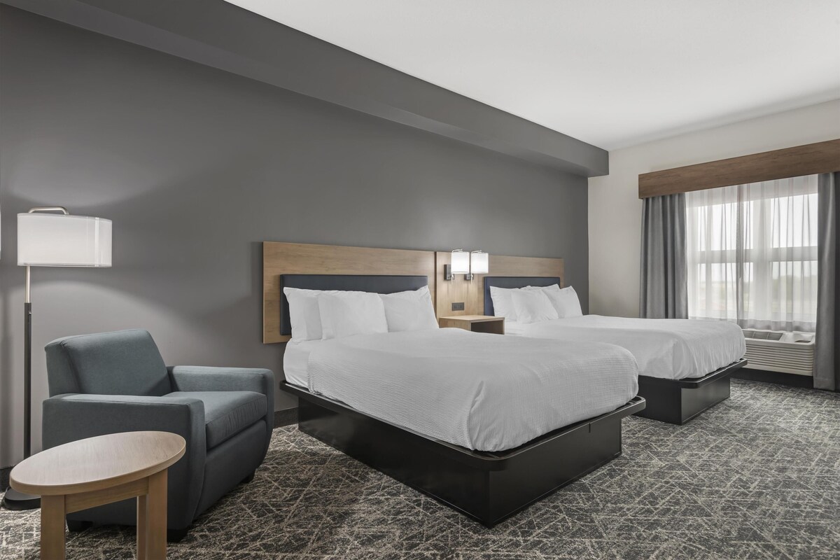 A hotel room with two beds, a desk, a chair, a lamp, and a window with curtains.