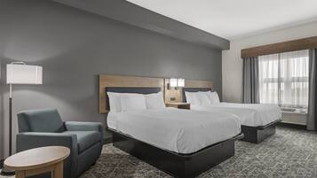 A hotel room with two beds, a desk, a chair, a lamp, and a window with curtains.