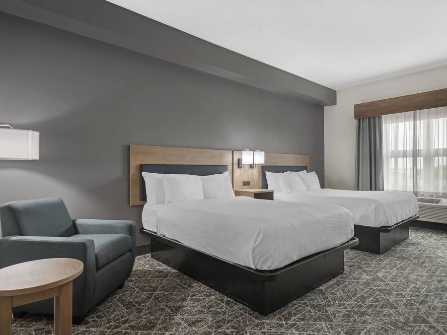 A hotel room with two beds, a desk, a chair, a lamp, and a window with curtains.