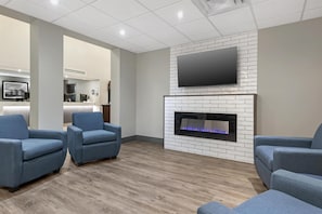 A modern living room with a flat-screen TV mounted above a fireplace, two blue armchairs, and a wooden floor.