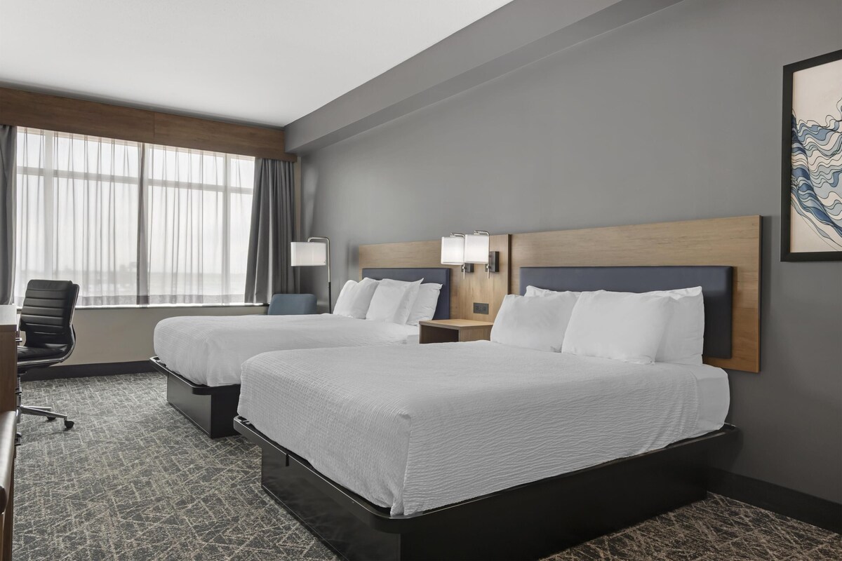 A hotel room with two beds, a desk, a chair, and a window with curtains.