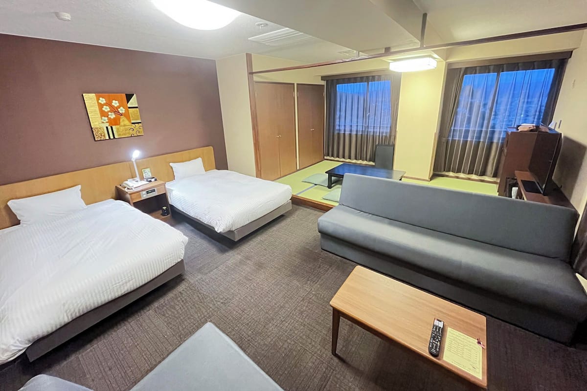 A hotel room with two beds, a sofa, a small table, and a desk with a lamp.