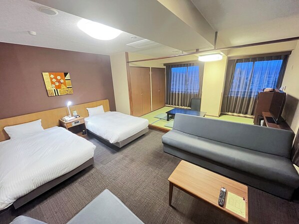 A hotel room with two beds, a sofa, a small table, and a desk with a lamp.