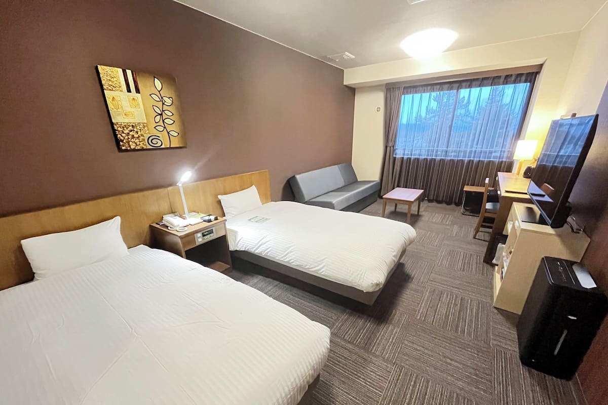 A hotel room with two beds, a desk with a computer, a TV, and a window with curtains.