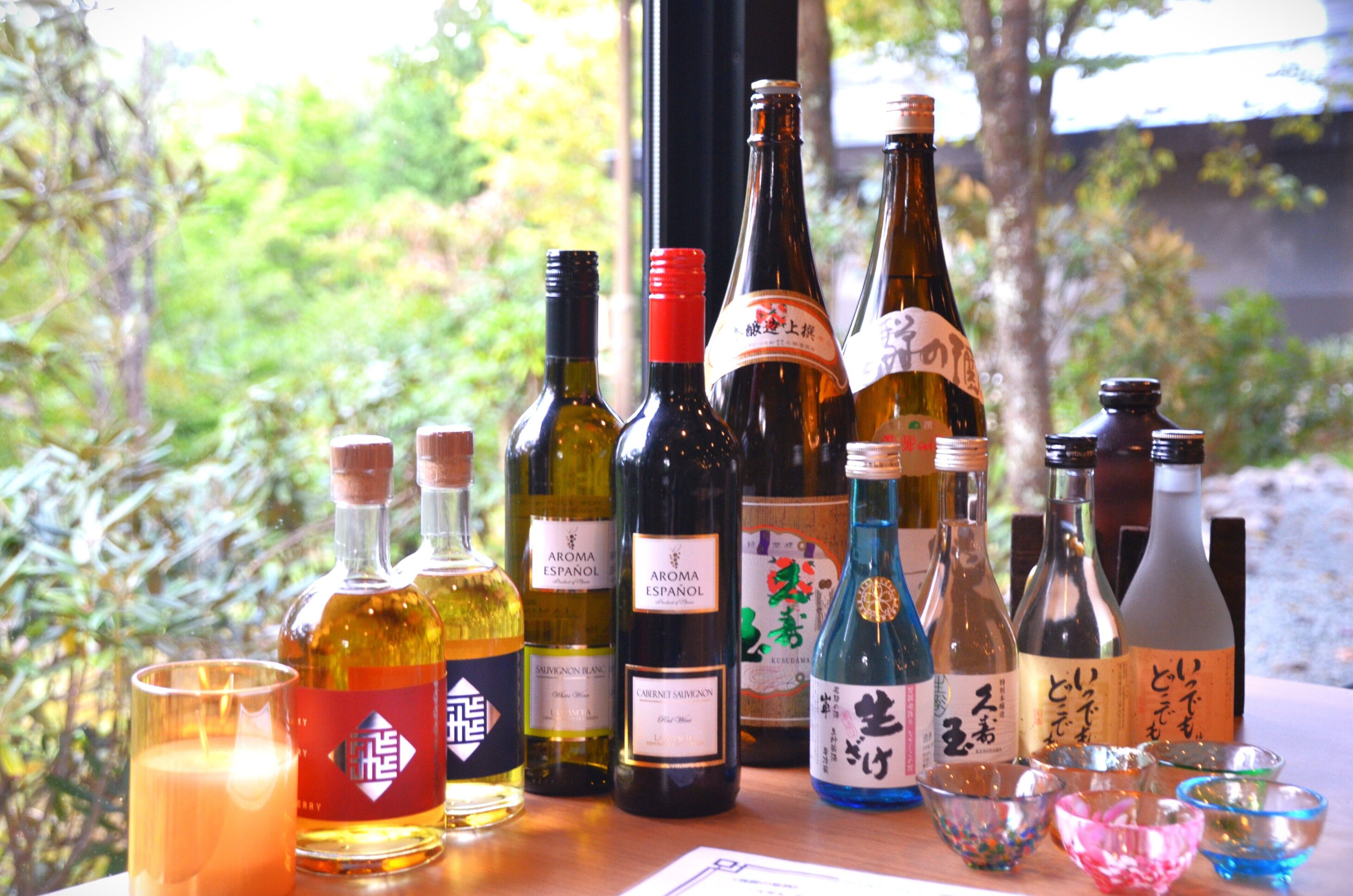 A variety of bottles and glasses on a table with a natural outdoor background.
