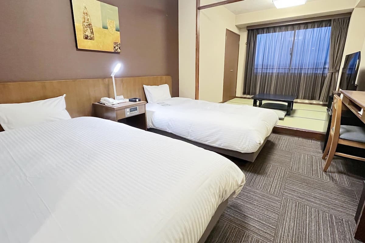 A hotel room with two beds, a desk, a chair, a TV, and a window with curtains.