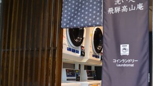 Et møntvaskeri med flere vaskemaskiner og tørretumblere, en træafskærmning og et banner med japansk tekst.