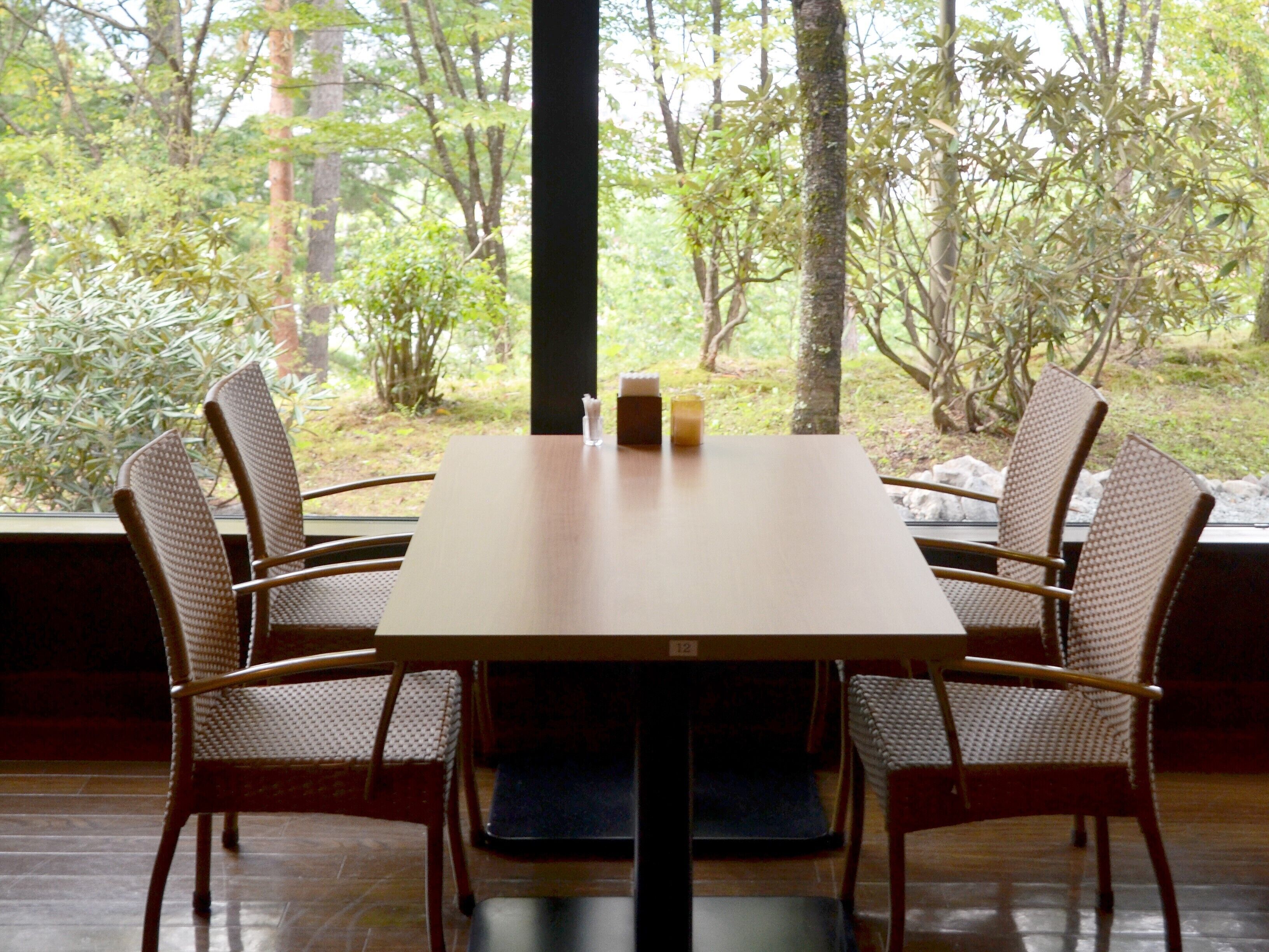 A dining table with four wicker chairs, a candle, and a small vase.