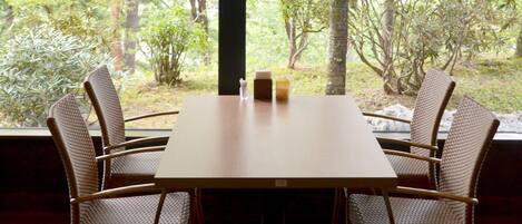 A dining table with four wicker chairs, a candle, and a small vase.