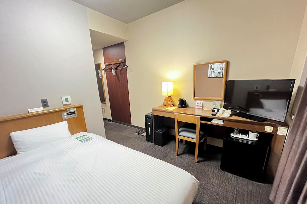 A hotel room with a bed, a desk with a computer, a TV, and a small table with a cup and saucer.