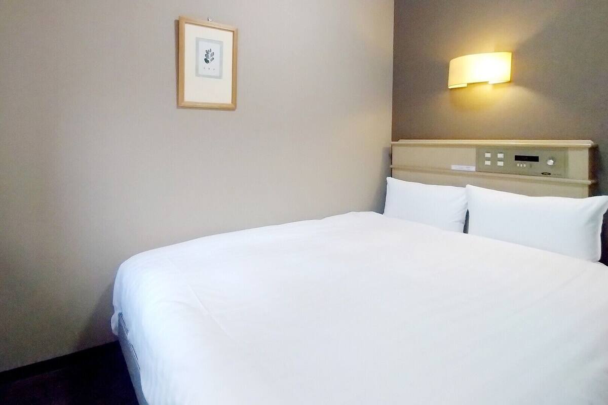 Une chambre d’hôtel avec un lit, une table de chevet, une lampe fixée au mur et un tableau encadré accroché au mur.