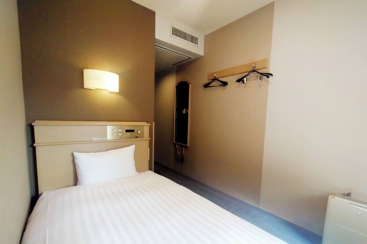 Une chambre d’hôtel équipée d’un lit, d’une lampe de chevet, d’un panneau de commande, d’un porte-manteau et d’un radiateur.