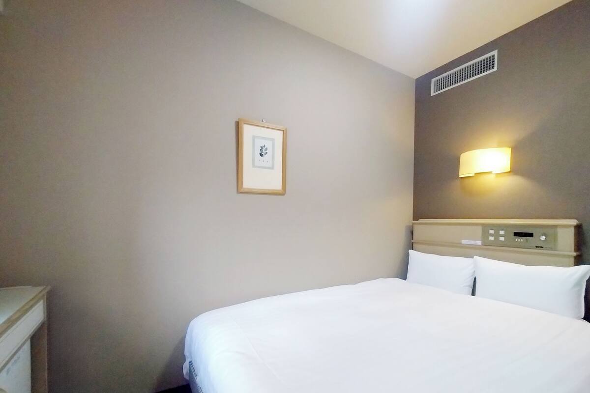 Une chambre d’hôtel avec un lit, une table de chevet, une lampe fixée au mur et un tableau encadré.
