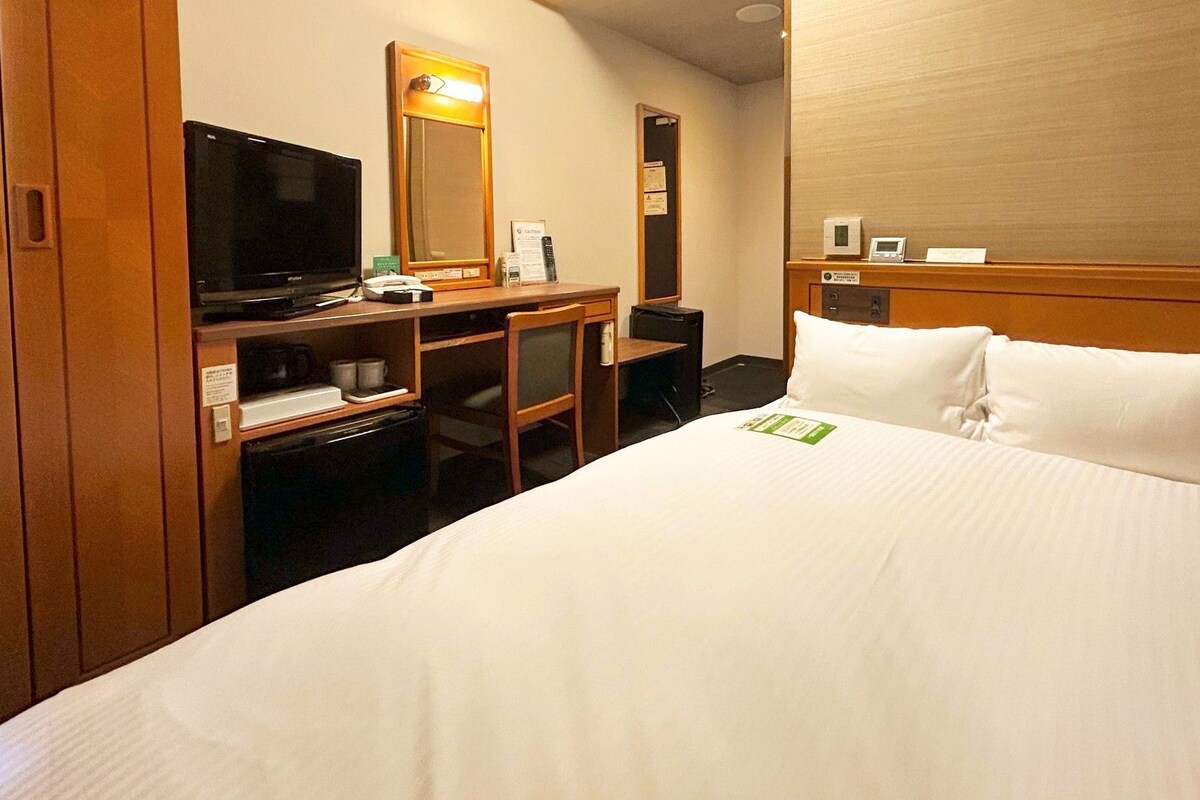 A hotel room with a bed, a desk with a computer, a television, and a minibar.